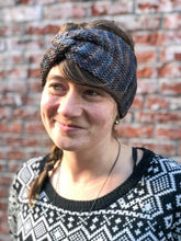 Load image into Gallery viewer, Knitted headband with knotted front shown on a model against a brick background.  The headband in a blend of light blues and browns.
