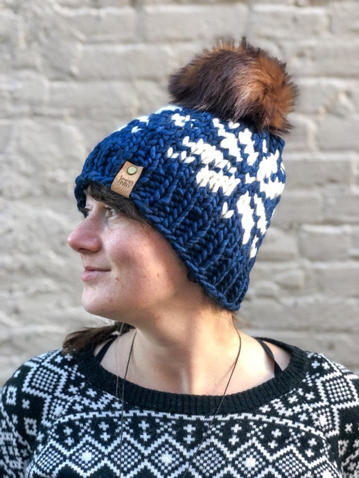 Snowflake Beanie in Navy with white snowflake and brown pom.  It is shown here on a model.