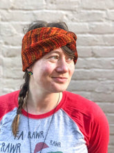 Load image into Gallery viewer, Knitted headband with knotted front shown on a model against a white brick background.  The headband is a blend of reds and oranges.
