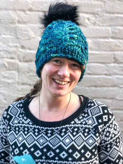 Fossil Beanie in green/blue with black pom.  It is shown here on a model.