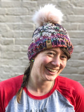 Load image into Gallery viewer, Snowflake Beanie in rainbow with white snowflake and pink pom.  It is shown here on a model.
