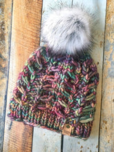 Load image into Gallery viewer, Fossil Beanie in rainbow with gray pom.  It is shown here in a flat lay against a wooden background.
