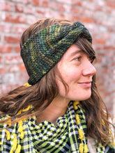 Load image into Gallery viewer, Knitted headband with knotted front shown on a model against a brick background.  The headband is a blend of greens and blues.
