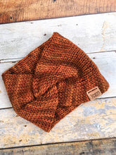 Load image into Gallery viewer, A knit headband with knot in the front shown against a wooden background.  The headband is a blend of reds and oranges.
