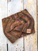 Load image into Gallery viewer, A knit headband with knot in the front shown against a wooden background.  The headband is a blend of golds, greens, and purples.
