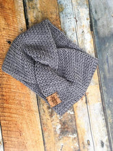 Load image into Gallery viewer, A knit headband with knot in the front shown against a wooden background.  The headband is a light gray.
