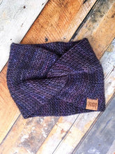 Load image into Gallery viewer, A knit headband with knot in the front shown against a wooden background.  The headband is a blend of dark blues and purples.
