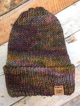Load image into Gallery viewer, The Hadrosaur Hat is a lightweight, double layered slouchy beanie with folded brim.  It is shown here in gold/purple/brown in a flat lay.
