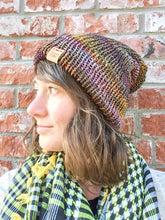 Load image into Gallery viewer, The Hadrosaur Hat is a lightweight, double layered slouchy beanie with folded brim.  It is shown here in gold/purple/brown on a model.

