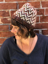 Load image into Gallery viewer, The Find Your Way Beanie has a chevron stripe pattern in two colors.  It is shown here on a model in white and brown.
