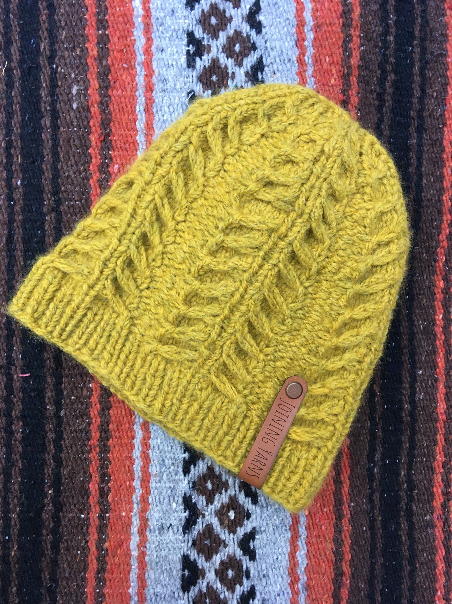 The Fossil Beanie is shown here in bulky weight yarn in a mustard color in a flat lay.