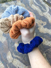 Load image into Gallery viewer, The Cotton Scrunchy is a simple knit hair accessory.  They are shown here on a wrist like a bracelet with 3 held in a hand.
