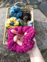 Load image into Gallery viewer, A basket of knit scrunchies in the background with a hand holding a magenta scrunchie in the foreground.

