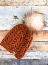 Load image into Gallery viewer, Fossil Beanie in copper with white and brown pom.  It is shown here in a flat lay.
