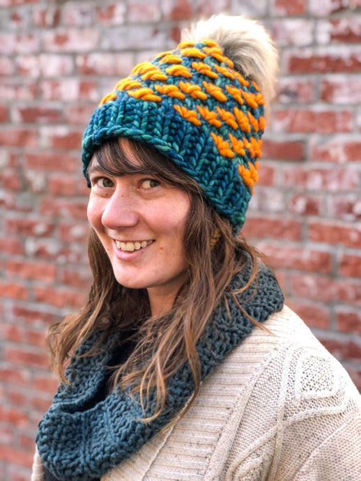 Lotus Beanie in teal with orange flowers and gray pom.  It is shown here on a model.
