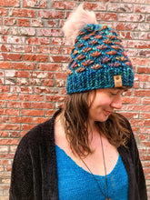Load image into Gallery viewer, Lotus Beanie in teal with brown flowers and pink pom.  It is shown here on a model.
