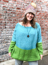 Load image into Gallery viewer, Lotus Beanie in beige with rainbow flowers and white/brown pom.  It is shown here on a model.
