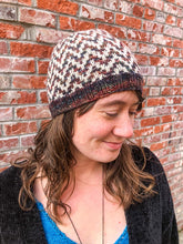 Load image into Gallery viewer, The Find Your Way Beanie has a chevron stripe pattern in two colors.  It is shown here on a model in white and dark rainbow.

