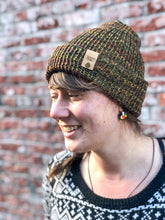 Load image into Gallery viewer, The Hadrosaur Hat is a lightweight, double layered slouchy beanie with folded brim. It is shown here in gold/purple/brown on a model.
