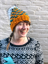 Load image into Gallery viewer, Lotus Beanie in orange with teal flowers and white pom.  It is shown here on a model.
