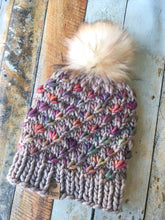 Load image into Gallery viewer, Lotus Beanie in beige with rainbow flowers and white/brown pom. It is shown here in a flat lay.
