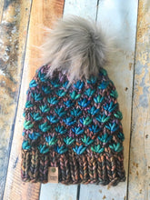 Load image into Gallery viewer, Lotus Beanie in brown with teal flowers and gray pom.  It is shown here in a flat lay.

