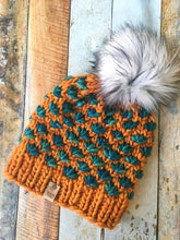 Load image into Gallery viewer, Lotus Beanie in orange with teal flowers and white pom.  It is shown here in a flat lay.
