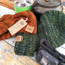 Load image into Gallery viewer, A folded brim slouchy beanie in flat lay with a knotted head wrap.  The hat has green and blue tones.  The wrap has orange tones.  In the background are camping supplies:  a kettle and a lantern.  And a headlamp is in the foreground.
