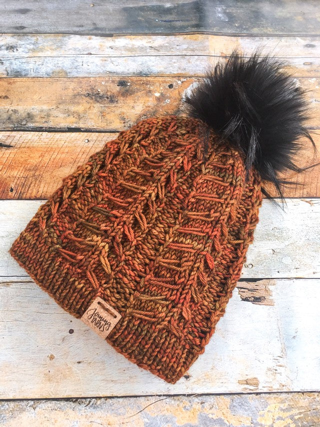 Fossil beanie in flat lay in orange color with black pom.