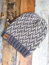 Load image into Gallery viewer, The Find Your Way Beanie has a chevron stripe pattern in two colors.  It is shown here in a flat lay in white and gray.
