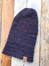 Load image into Gallery viewer, The Hadrosaur Hat is a lightweight, double layered slouchy beanie with folded brim. It is shown here in dark blue/purple in a flat lay with brim unfolded.
