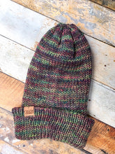 Load image into Gallery viewer, The Hadrosaur Hat is a lightweight, double layered slouchy beanie with folded brim. It is shown here in light rainbow (arco iris) in a flat lay with brim folded.
