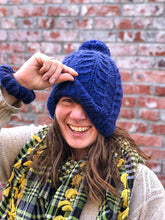 Load image into Gallery viewer, Fossil Beanie in navy with matching yarn pom.  It is shown here on a model.
