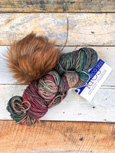 Load image into Gallery viewer, Skein of rainbow yarn with brown pom.
