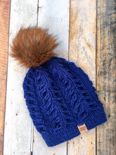 Load image into Gallery viewer, Fossil Beanie in navy with brown pom.  It is shown here in a flat lay.

